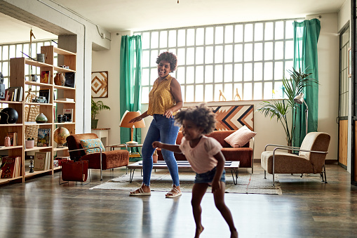 Energetic 3 year old Afro-Caribbean girl doing aerobic dancing with her mid 20s mother in living room of family home.