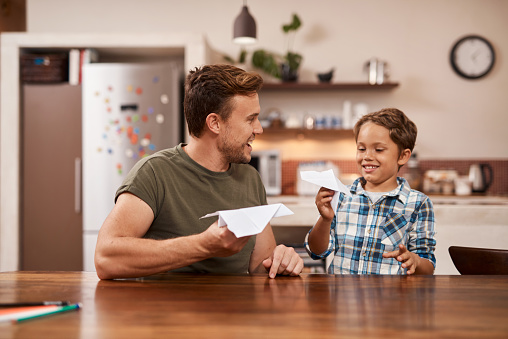 Cropped shot of a man and his young son playing with paper planes at home