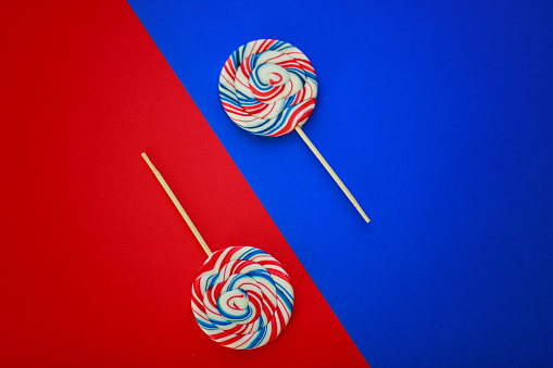 Flat lay of two lollipops out of their packages placed on top of vibrant red and blue backgrounds in a diagonal.