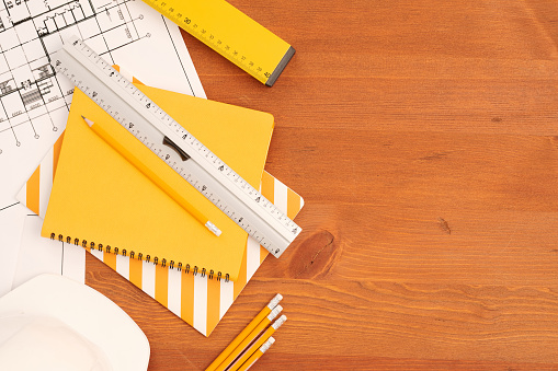 Flatlay of copybooks, rulers and pencils by unfolded blueprints with sketches of new building drawn by contemporary engineer