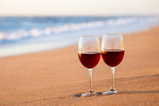 two glasses of red wine on the beach with sea on the background