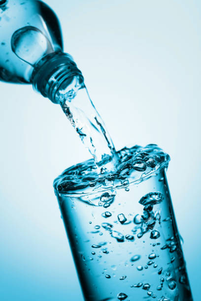 istock Pouring water from a bottle into glass on a blue background. 1274787259
