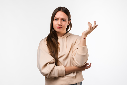 Studio shot of displeased girl with long chestnut hair, gesturing with raised palm, frowning, being displeased and confused with dumb question. Human emotions concept