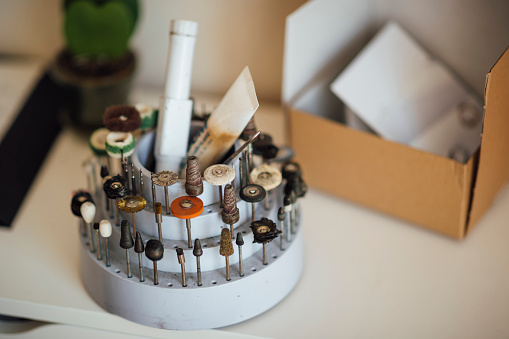 A close-up of a jewelers tool attachments placed in a container on a workbench.