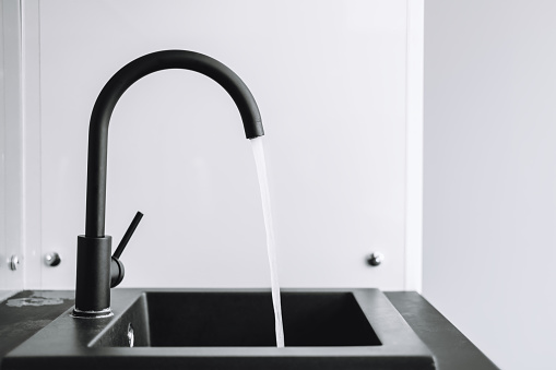Close-up on the kitchen sink as a woman turns on the cold water tap in her home.