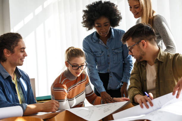 istock Group of design students sitting in classroom and examining blueprint homework project. 1274853191