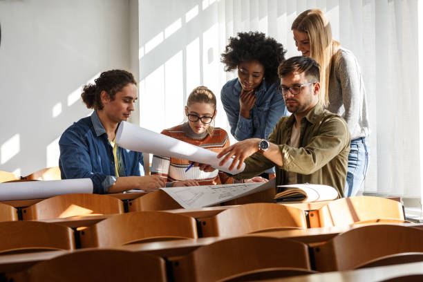 istock Group of design students sitting in classroom and examining blueprint homework project. 1274853291