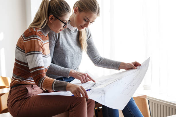 istock Two female design students sitting in classroom and examining blueprint. 1274854753
