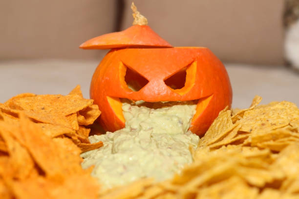 Halloween Food Carved pumpokin filled with guacamole and tortilla chips. Halloween party food. Selective focus. throwing up pumpkin stock pictures, royalty-free photos & images