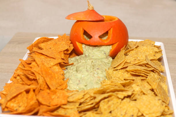 Halloween Food Carved pumpokin filled with guacamole and tortilla chips. Halloween party food. Selective focus. throwing up pumpkin stock pictures, royalty-free photos & images