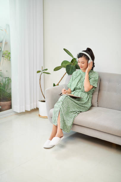 istock mage of focused asian woman using headphones and writing down notes while sitting on sofa at home 1274869393