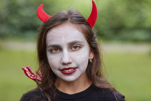 Close up portrait of smiling teenage girl wearing devil costume and face paint looking at camera outdoors