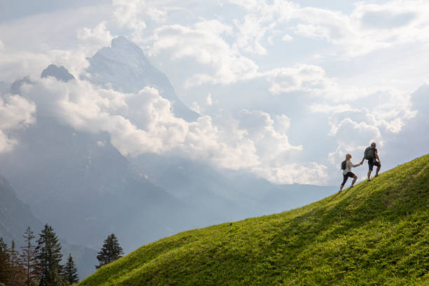 Aerial view of hiking couple traversing alpine meadow in the morning Holding hands, they chat and look off to distant scene, Swiss Alps in distance grindelwald photos stock pictures, royalty-free photos & images