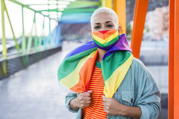 young woman wearing gay pride mask, flag outdoor - lgbt rights, diversity, tolerance and gender identity concept - life events laughing women latin american and hispanic ethnicity imagens e fotografias de stock
