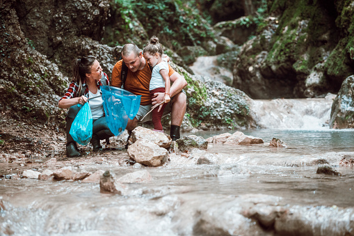 Young family cleaning small river from garbage