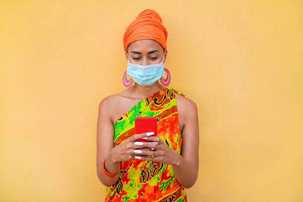 istock Young african woman using mobile phone while wearing protective face mask during coronavirus outbreak 1274948117