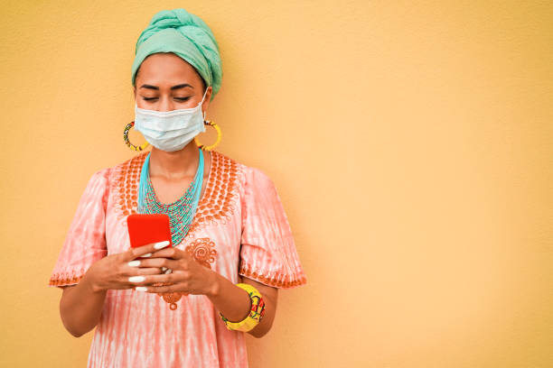 istock Young african woman using mobile phone while wearing protective face mask during coronavirus outbreak 1274948413