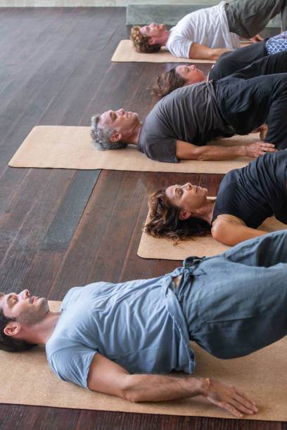 ブリッジポーズに横たわるヨガを練習している木製の床の人々の多様なグループ - セトゥバンダサルバンガサナ。健康的なライフスタイル - lying down moving down pilates yoga ストックフォトと画像