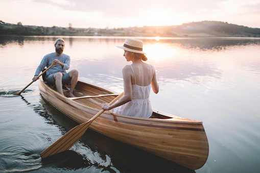 Couple enjoy time outdoors in the canoe on the sunset lake.