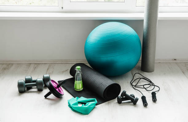 group of different exercising equipment on white home gym floor. fitness ball, round foam roller, resistance exercise latex band, jumping rope, dumbbells, yoga mat. fit lifestyle concept. - man made material fotos imagens e fotografias de stock