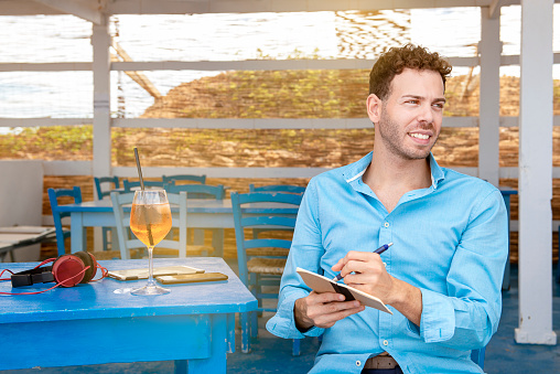 Left-handed young man sitting at beach bar writing doing his homework concept of smart-working outdoor