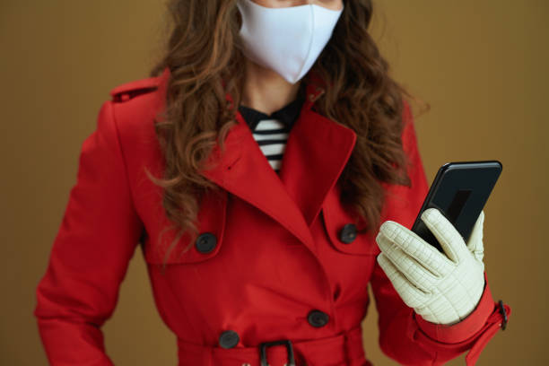 mujer de moda en el abrigo usando la aplicación del teléfono contra el fondo marrón - easy money audio fotografías e imágenes de stock