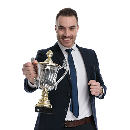 Happy businessman presenting trophy and smiling while standing on white studio background