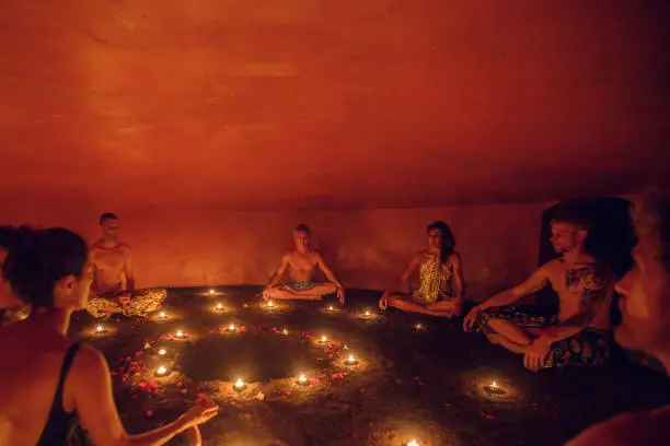 Group of people inside Mayan Temazcal- traditional steam sauna bath of Mesoamerican cultures. Diverse multiethnic people sitting around candle lights in circle and meditating