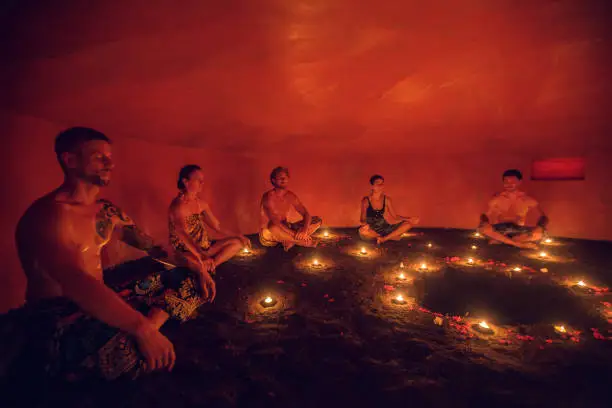 Photo of Group of people inside Mayan Temazcal- traditional steam sauna bath of Mesoamerican cultures. Diverse multiethnic people sitting around candle lights in circle in darkness and meditating