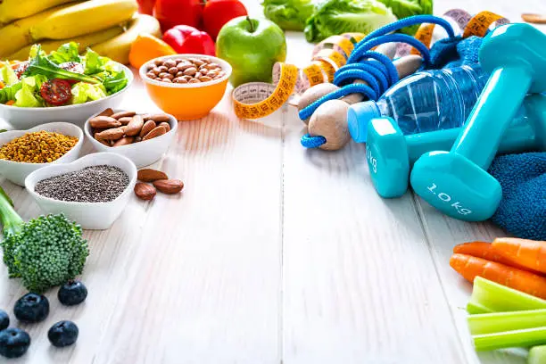 Photo of Sports and healthy food concept: fruits, vegetables, nuts, dumbbels and tape measure. Copy space