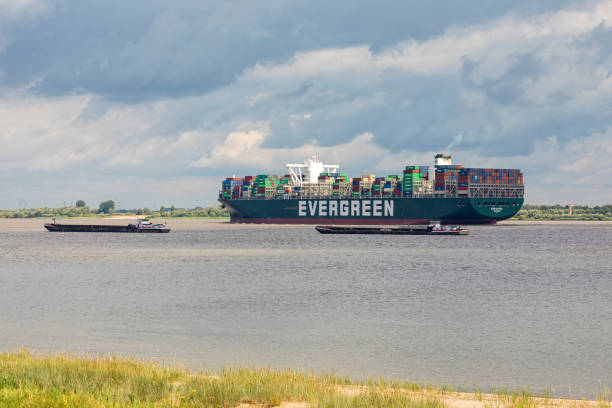 Stade, Germany - July 3, 2020: Container ship EVER GIFTED operated by EVERGREEN LINE and registered in Singapore leaving Hamburg on Elbe river passing moored riverboats