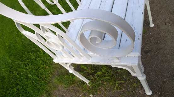 Detail of metal vintage white bench. Empty chair in the garden. Place for relaxation and inspiration. Concept of ecology and comfortable urban environment. Provence style outdoor furniture. Rest.