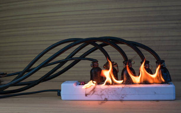 in fiamme multi socket con la striscia di alimentazione collegata con un mucchio di spine su sfondo legno - electricity fire circuit board short foto e immagini stock