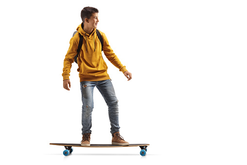 Full length shot of a male teenager in a yellow hoodie riding a longboard isolated on white background
