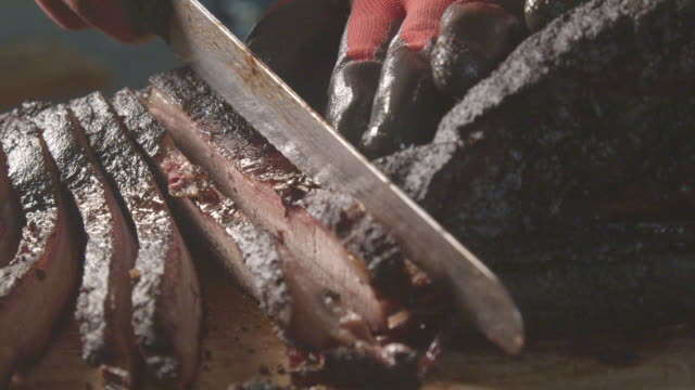 Gloved Hands Slowly Cutting Perfectly Cooked Texas Barbecue Style Beef Brisket on a Rustic Cutting Board