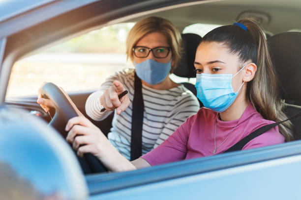 Teenager having driving lesson with female instructor during Covid 19 A teenage girl with protective mask sitting behind the steering wheel of a car and listening to her mothers instructions as she drives. driving test photos stock pictures, royalty-free photos & images