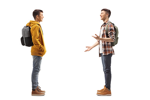 Full length profile shot of two male teenage students having a conversation isolated on white background
