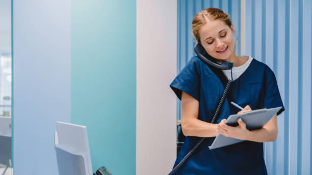 mujer practicante caucásica trabajando en la recepción mientras contesta llamadas telefónicas y programa citas en la clínica médica - secretary fotografías e imágenes de stock