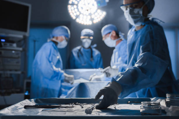 herramientas quirúrgicas acostadas sobre la mesa mientras el grupo de cirujanos en el paciente de fondo en el teatro quirúrgico - cirugía fotos fotografías e imágenes de stock