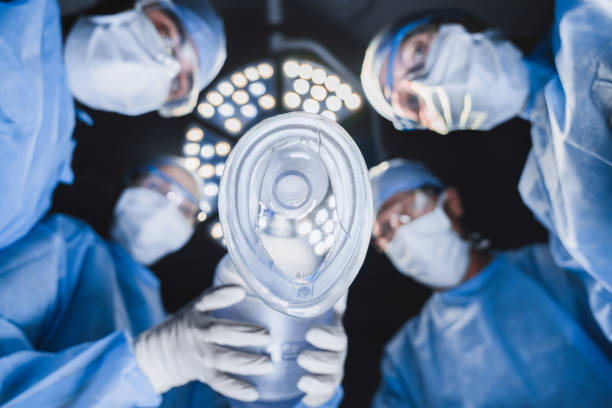 vista de ángulo bajo del anestesista sosteniendo la máscara de oxígeno sobre el paciente en la sala de cirugía con un equipo de profesionales cirujanos. - anestesista fotografías e imágenes de stock