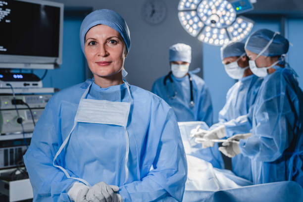 ritratto di chirurgo donna adulta in sala operativa con il suo team sullo sfondo. - surgeon isolated paramedic operating room foto e immagini stock