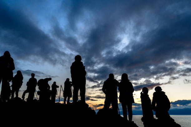 Faceless group of people on top of a mountain watching sunset, silhouette of group of people taking pictures outside during sunrise or sunset stock photo