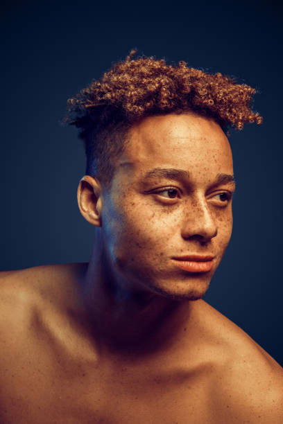 istock Freestyle. Freckled guy bare body standing isolated on dark red in yellow light looking aside curious close-up 1275106932