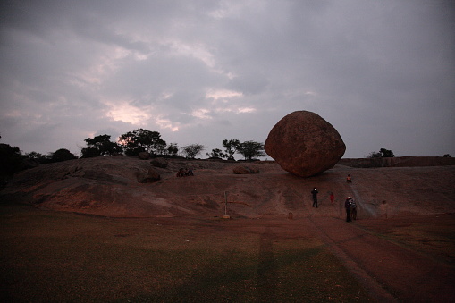 Tourists visiting a gigantic balancing  granite boulder Krishna's Butterball under sunset in Mahabalipuram, Tamil Nadu, India