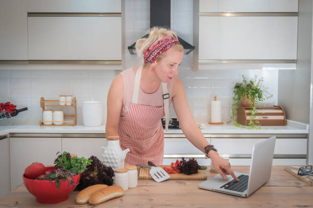 istock Smiling woman using laptop while making healthy appetizer in the kitchen. 1275165357