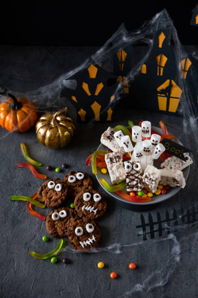 istock Modern Halloween background. Halloween candy bar: funny monsters made of biscuits with chocolate and ghosts marshmallow close-up on the table. Halloween party decoration. Trick or treat concept. 1275174894