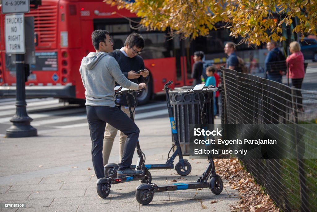 Two men choosing electric scooter for city ride. Autumn fall season. Washington, DC, USA - October, 31, 2018: Two men choosing electric scooter for city ride. Red city bus on a background.  Autumn fall season. Electric Push Scooter Stock Photo