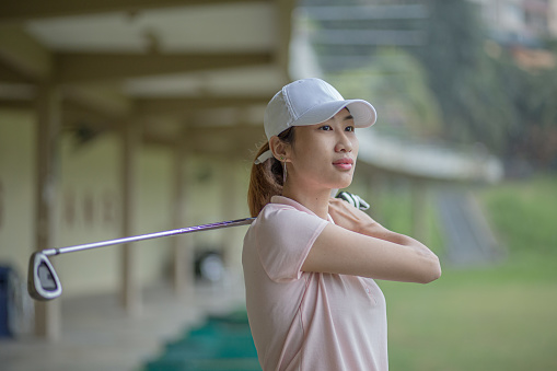 Young Asia Chinese woman golfer teeing off and swing her driver at golf driving range during rainy day.