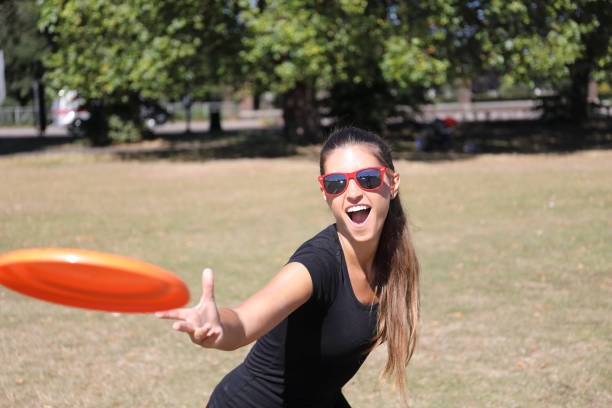 Beautiful Russian outdoor girl model throwing an orange plastic toy frisbee on open grassland on a sunny summer's day. Healthy outdoor activity.