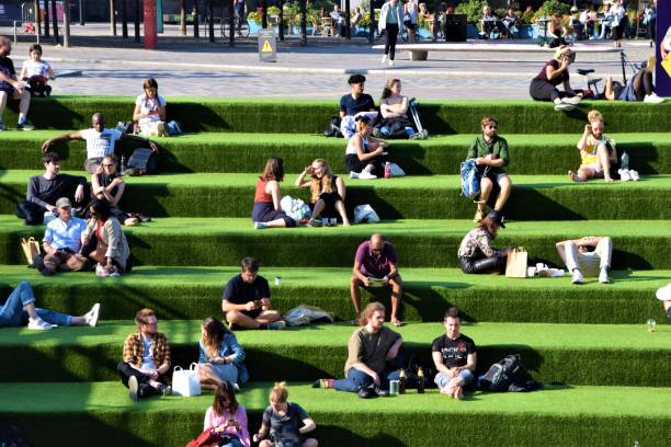 People sitting on green steps at Granary Square, King's Cross, London London, United Kingdom - September 2020: People sitting on the steps at Granary Square in King's Cross on a sunny day granary stock pictures, royalty-free photos & images